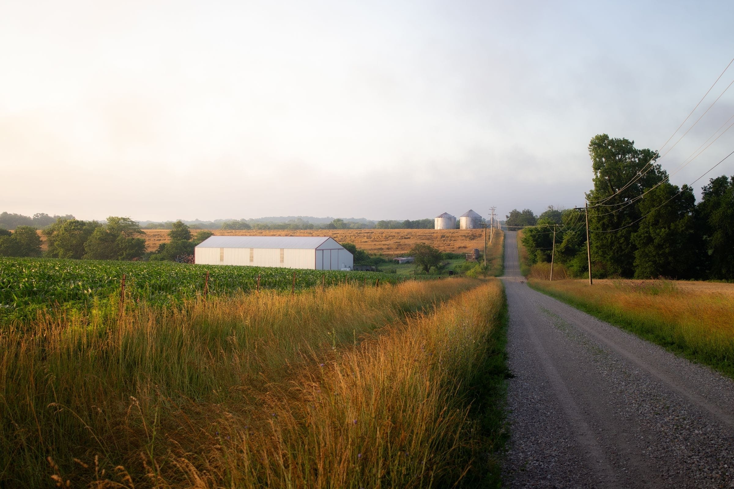 Towing Dunlap IL: gravel farm road beside fields with a white barn and grain bins, the kind of road our trucks cover around Dunlap